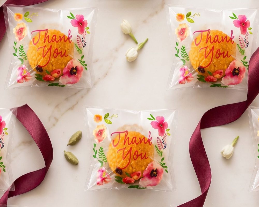 Laddoo in floral Thank You pouches on marble with a burgundy ribbon
